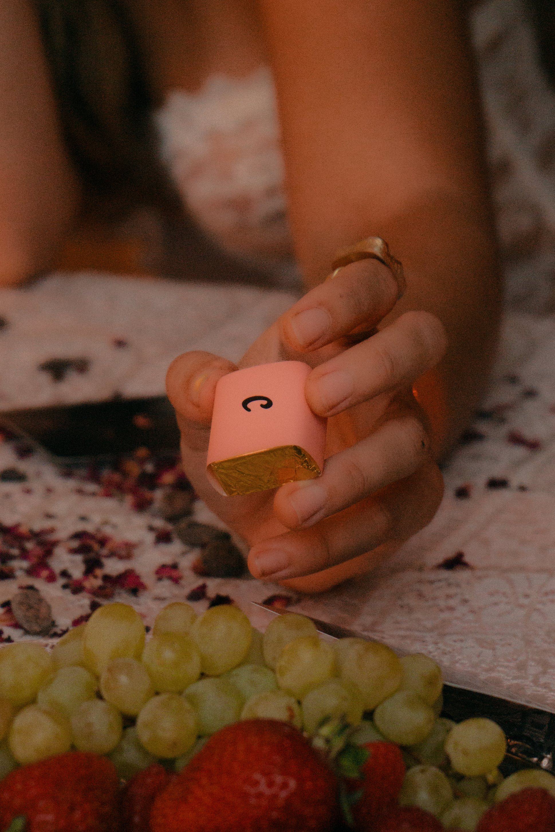 Hand holding a CravedThis chocolate above a spread of fruit and rose petals